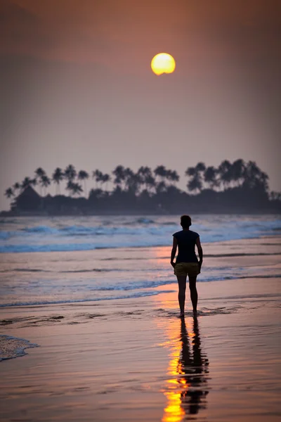 Vrouw loopt op het strand bij zonsondergang — Stockfoto