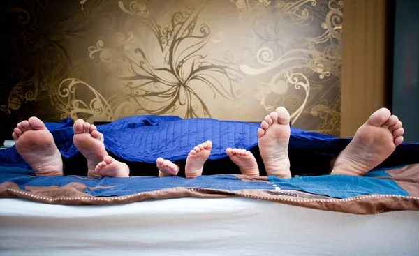 Quattro paia di gambe della famiglia felice a letto - padre, madre a — Foto Stock