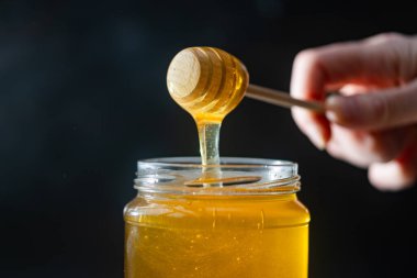 organik bal, ahşap bir kaptan cam bir kavanoza damlıyor.,