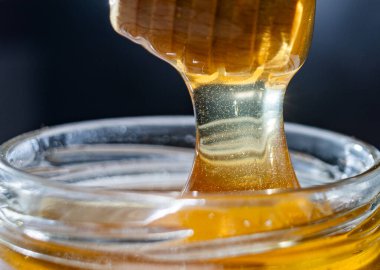 organik bal, ahşap bir kaptan cam bir kavanoza damlıyor.,