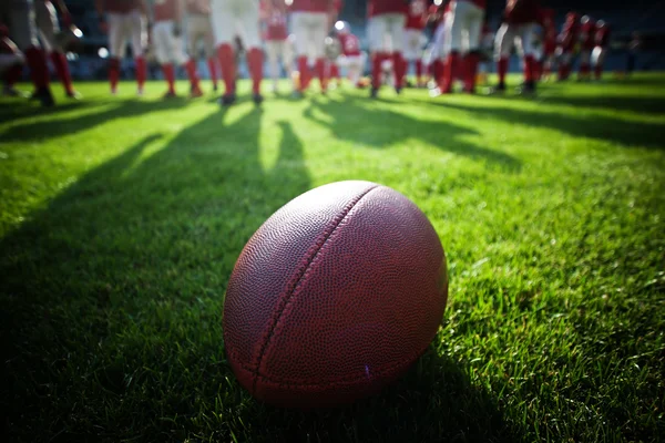 Close up of an american football on the field, players in the ba — Stock Photo, Image