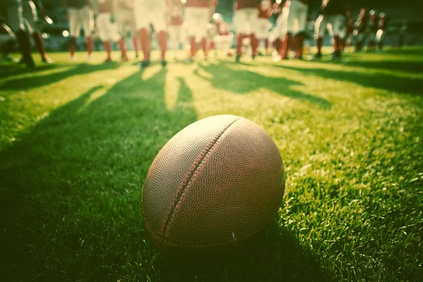 Close up of an american football on the field, players in the ba — Stock Photo, Image