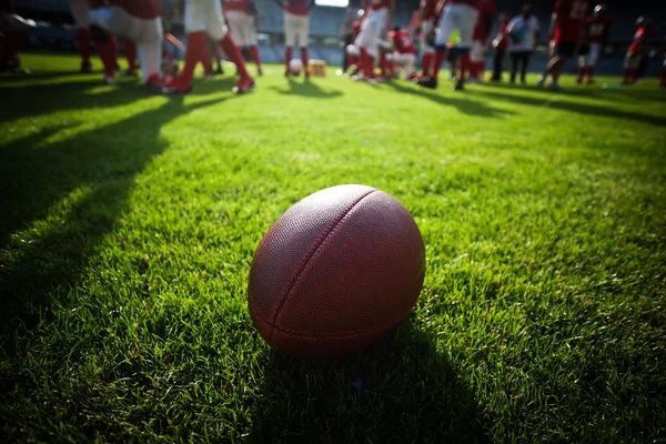 Close up of an american football on the field, players in the ba — Stock Photo, Image