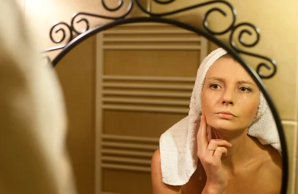 Middle-aged woman checking her face in bathroom mirror after sho — Stock Photo, Image