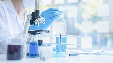 Tıbbi ya da bilimsel araştırmacı ya da insan doktoru laboratuarda bir test tüpü dolusu temiz çözeltiye bakıyor.