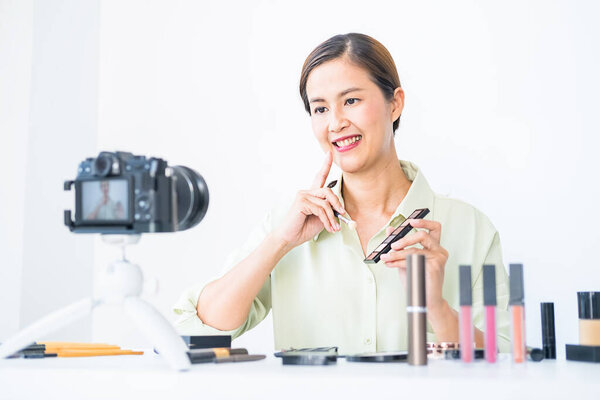 Женщина делает видео для своего блога о косметике с помощью цифровой камеры. Молодая блоггер на экране камеры держит косметику.