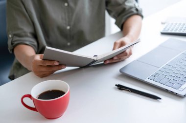 İş kadını iş yerinde ya da evde koltukta oturup dizüstü bilgisayar üzerinde çalışıyor ve şirket için iş planı ve stratejiler oluşturmak için çizelgeler ve grafikler üzerindeki verileri analiz ediyor ve kağıtlara yazıyor. İş konsepti.