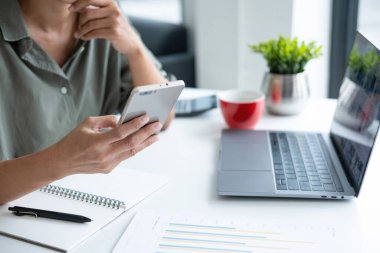 İş kadını iş yerinde ya da evde koltukta oturup dizüstü bilgisayar üzerinde çalışıyor ve şirket için iş planı ve stratejiler oluşturmak için çizelgeler ve grafikler üzerindeki verileri analiz ediyor ve kağıtlara yazıyor. İş konsepti.