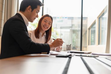 İş yerinde birlikte çalışan erkek ve kadın işadamları, stratejiler, planlar, analitik ilerleme ve finansal istatistikler hakkında tartışıyor ve masa başında elinde kalem ve hesap makinesi bulunan grafik belgelerine işaret ediyorlar. İş ve Takım Çalışması konsepti.