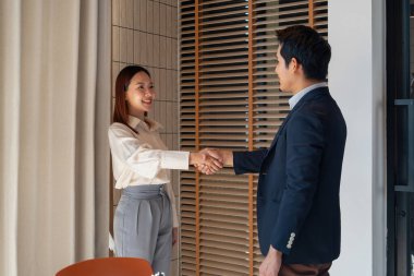 İş adamı ve iş kadını resmi giysiler içinde iş yerinde birlikte çalışıyorlar. Ayakta duruyorlar, anlaşarak el sıkışıyorlar ve işlerini tamamlıyorlar. İş adamları birlikte çalışmaktan memnuniyet duyar.. 