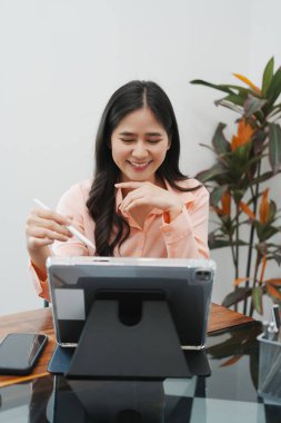 Masasında dizüstü bilgisayar ve kağıtlarla oturan genç ve güzel iş kadını ofiste ya da iş yerinde mutlu, sevinçli ve başarılı, tamamlanmış işi kutluyor. İş, başarı kavramı.