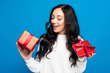 Kazaklı mutlu kadın mavi üzerine izole edilmiş Noel hediyesi kutusuna bakıyor.