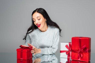 Heyecanlı kırmızı dudaklı kadın, hediye kutusunun yanında, gri renkte izole edilmiş.