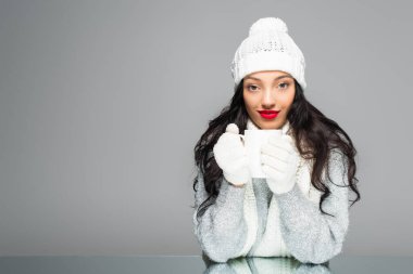 Kışlık kıyafetli neşeli ve esmer bir kadın gri bardakta izole edilmiş bir fincan tutuyor.