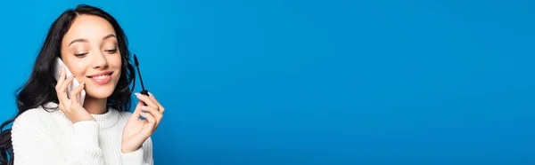 Усміхнена Брюнетка Жінка Тримає Щітку Туші Розмовляє Смартфоні Ізольовано Синьому — стокове фото