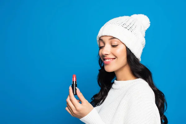 Sonriente Morena Mujer Sombrero Sosteniendo Lápiz Labial Aislado Azul —  Fotos de Stock