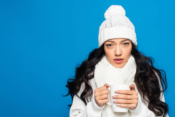 young woman in knitted hat and scarf holding cup while freezing isolated on white 