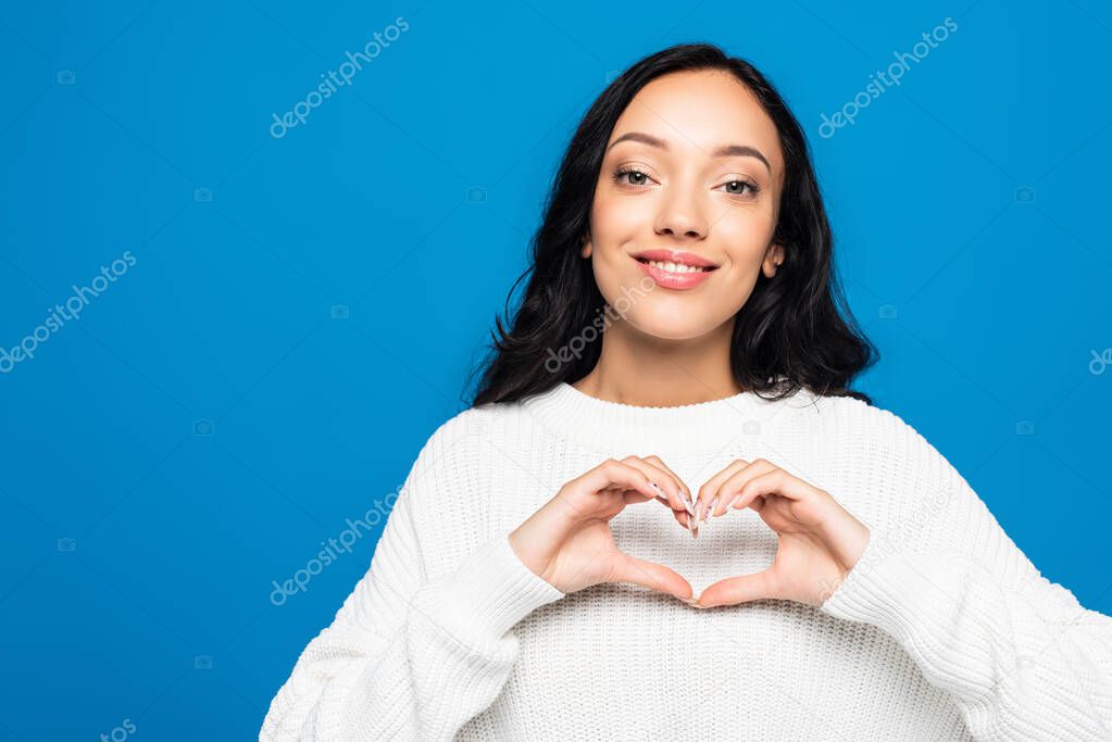 brunette woman showing heart sign with hands isolated on blue