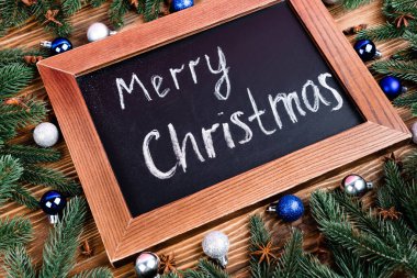 Kahverengi ahşap arka planda çam dalları, mücevherler ve anason yıldızlarının yanında mutlu noel yazıları olan kadife tahtası.