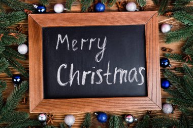 Kahverengi ahşap zemin üzerinde mutlu noel harfleri, çam dalları, takılar ve anason yıldızları olan karatahta manzarası