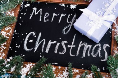 Karatahtaya yakından bak. Mutlu noel yazmaları, az hediye, çam dalları ve yapay kar.