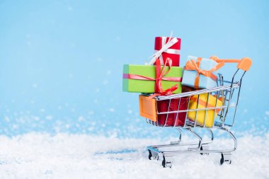 Surface level of shopping trolley with bunch of little gift boxes on blurred background, new year concept clipart