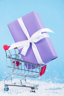 Close up view of little gift in shopping trolley on blue background, new year concept clipart