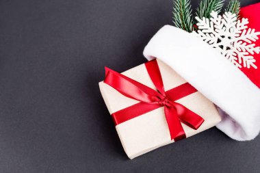 Noel Baba şapkası, dekoratif kar tanesi ve siyah arka planda çam dalı olan hediye manzarası, yeni yıl konsepti.