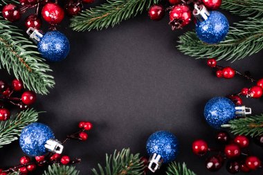 Çam dalları, yapay böğürtlenler ve siyah arkaplanda noel topları.