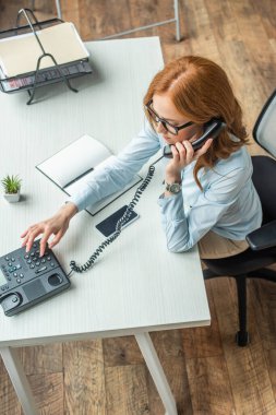 İş yerinde otururken ev telefonundan arayan kızıl saçlı iş kadınının genel görünümü