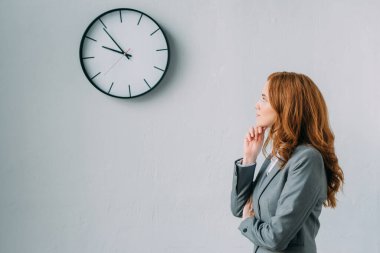 Düşünceli bir iş kadınının gri duvar saatine bakışının yan görüntüsü