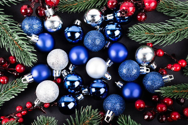 Top view of christmas balls, red beads and pine branches on black background