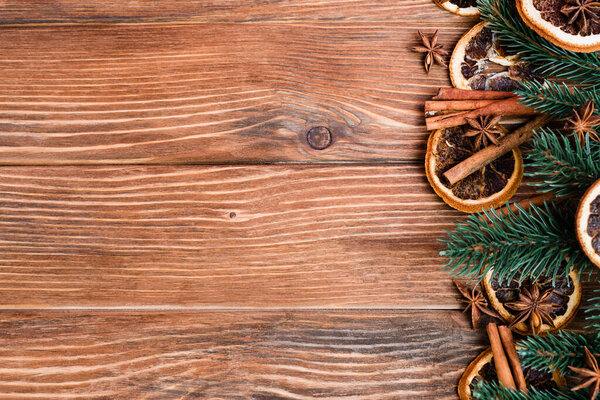 Вид сверху на анисовые звезды, сухие оранжевые слайсы, палочки камамона и ветки сосны на коричневом деревянном фоне