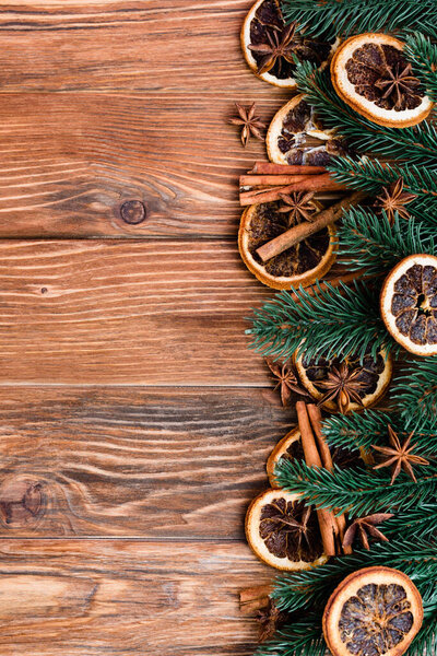 Top view of dry orange slices, anise stars, cinnamon sticks and pine branches on brown wooden background