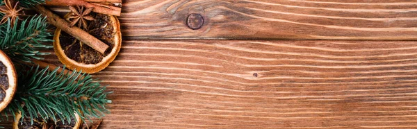 Top view of pine branch, dry orange slices, cinnamon sticks and anise stars on brown wooden background, banner