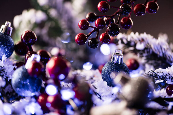 Close up view of red beads and bauble with blurred pine branches on background, new year concept