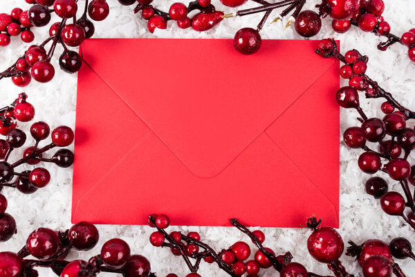 Top view of red envelope near branches with artificial berries on white textured background