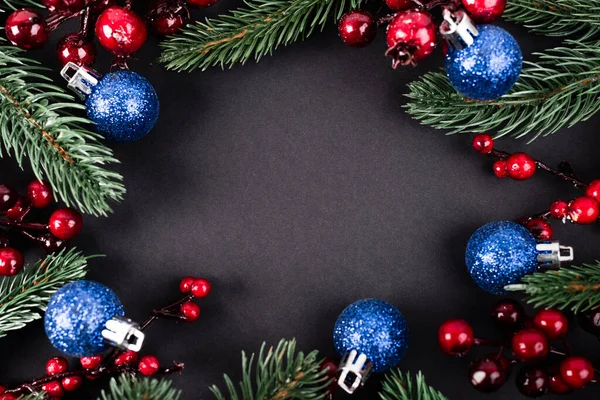 Çam dalları, yapay böğürtlenler ve siyah arkaplanda noel topları.