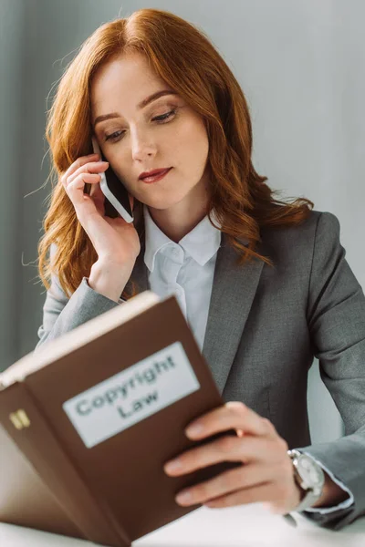 Redhead Δικηγόρος Μιλώντας Στο Κινητό Τηλέφωνο Ενώ Κοιτάζοντας Βιβλίο Γράμματα — Φωτογραφία Αρχείου