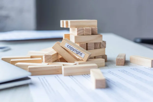 Close up view of blocks wood game constriction collapsing with copyright lettering with blurred workplace on background