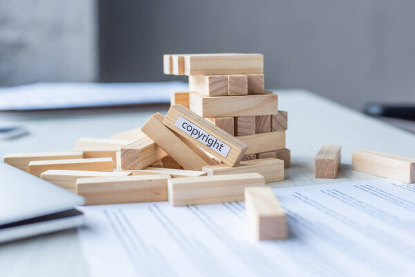 Close up view of blocks wood game constriction collapsing with copyright lettering with blurred workplace on background
