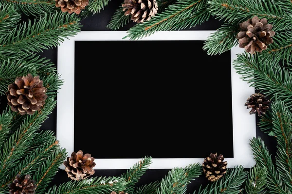 Flat lay with digital tablet, spruce branches and pine cones on black background, new year concept — Stock Image Flat Lay Digital Tablet Spruce Branches Pine Cones Black Background Stock Image