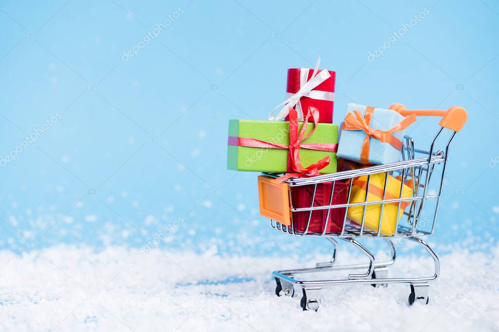 Surface level of shopping trolley with bunch of little gift boxes on blurred background, new year concept