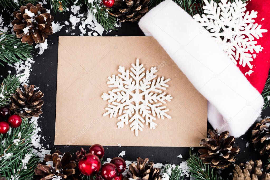 Top view of decorative snowflakes on envelope near pine cones, red beads and artificial snow on black background