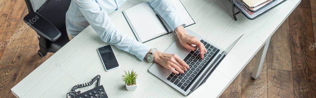 Cropped view of businesswoman typing on laptop, while sitting at workplace, banner