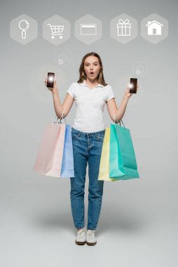Gri rengin yanında akıllı telefonlar ve alışveriş çantaları tutan şok olmuş bir kadın.
