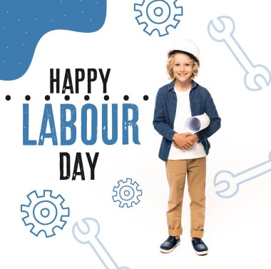 curly boy in safety helmet and costume of architect holding blueprint near happy labour day lettering on white  clipart