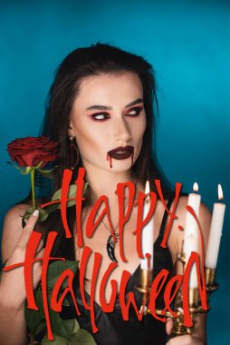 Yanan mumların yanında yüzü kan içinde genç bir kadın, gül ve mavi renkli Cadılar Bayramı harfleri.