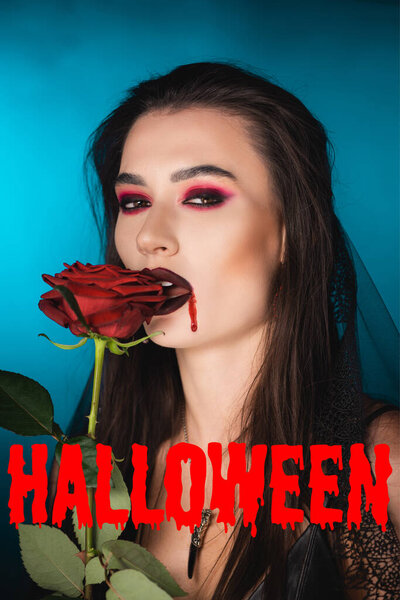 young and creepy woman with blood on face near red rose and halloween lettering on blue