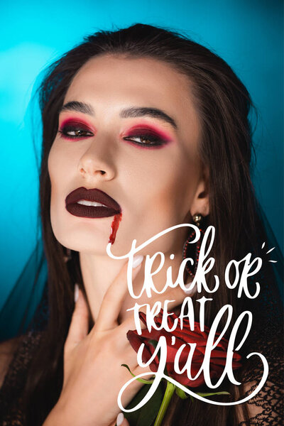 young woman with blood on face holding red rose near trick or treat lettering on blue